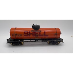 May include: An orange toy train car with the word "SHELL" in large, red letters. The car has a black base with wheels and metal detailing. The text "S.C.X. 1240" is also visible.