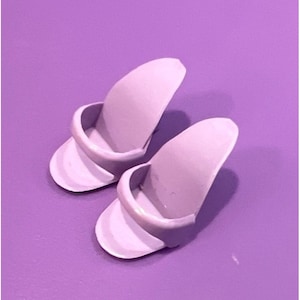 May include: A pair of lavender-colored plastic doll shoes. The shoes are open-toed and have a strap across the top.