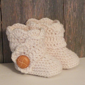 May include: A pair of crocheted baby booties in a cream color with a brown button on one bootie.