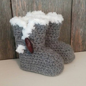May include: Gray crocheted baby booties with white faux fur lining and a brown wooden button.