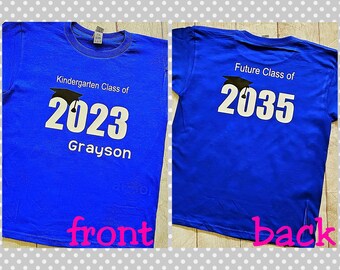 May include: Blue t-shirt with a black graduation cap and the text "Kindergarten Class of 2023 Grayson" on the front and "Future Class of 2035" on the back.