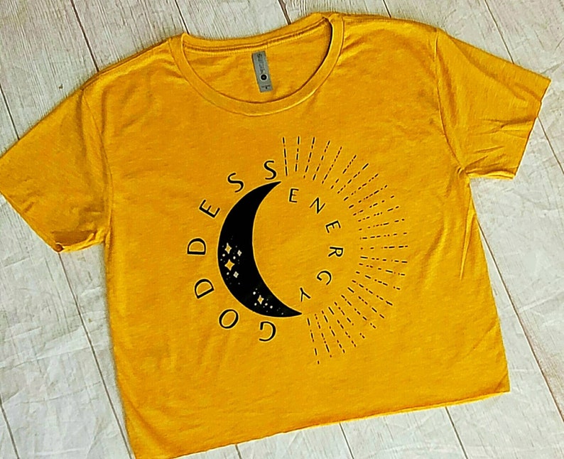 May include: A yellow cropped t-shirt with a black crescent moon graphic and the text "Goddess Energy" in a circular design.