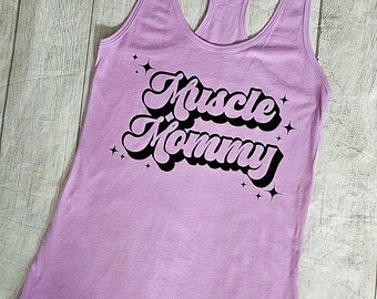 May include: A purple tank top with the text "Muscle Mommy" in a retro font with black outlines and white stars.