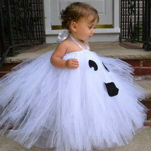 May include: A white tulle tutu with a ghost face design. The ghost has black eyes and a mouth. The tutu is perfect for a Halloween costume.