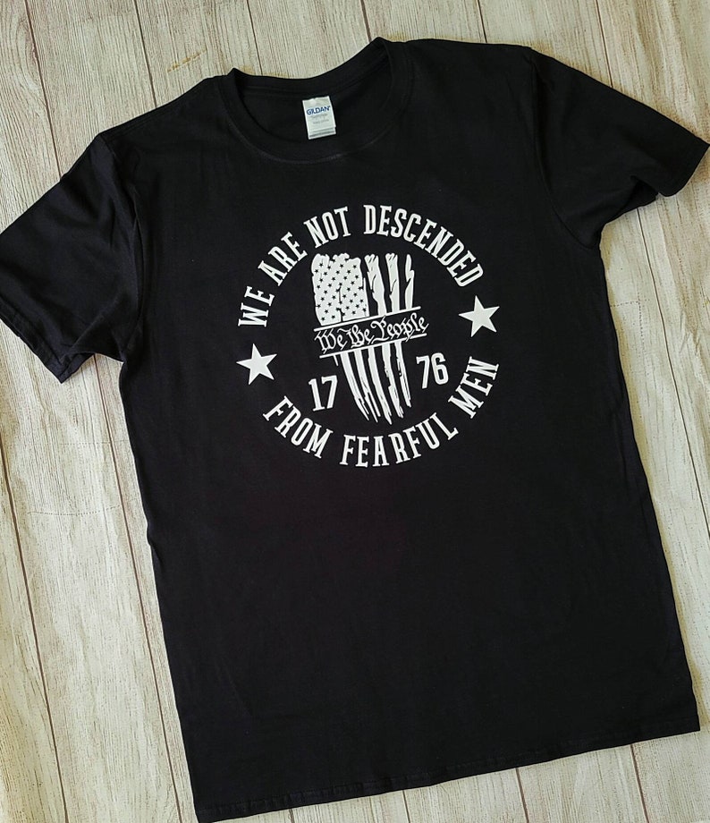 May include: Black t-shirt with a white graphic print of an American flag with the text "We Are Not Descended From Fearful Men" and "We The People" with the years 1776.