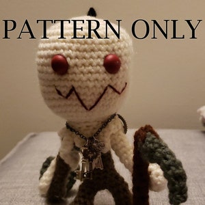 May include: Crocheted amigurumi doll with a white body, brown legs, and a green and brown staff. The doll has red eyes and a stitched smile. The doll is wearing a silver chain necklace with keys attached.
