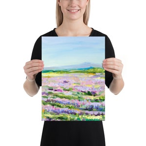 Op de afbeelding: Een schilderij van een veld met paarse bloemen met een bergketen op de achtergrond. De lucht is blauw en de bloemen zijn geschilderd in een losse, impressionistische stijl.