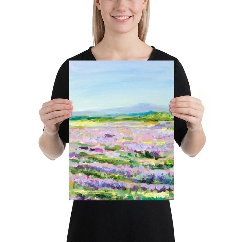 Op de afbeelding: Een schilderij van een veld met paarse bloemen met een bergketen op de achtergrond. De lucht is blauw en de bloemen zijn geschilderd in een losse, impressionistische stijl.