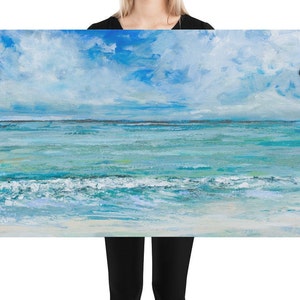 Op de afbeelding: Een schilderij van een zeelandschap met een blauwe lucht en witte wolken. De oceaan is lichtblauw met witte golven die aan de kust breken.