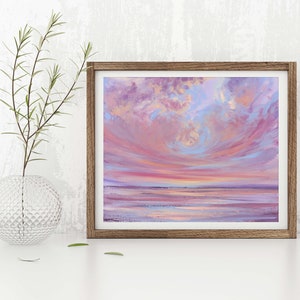 May include: A framed painting of a pink and purple sunset over a calm body of water. The sky is filled with fluffy clouds, and the water reflects the colors of the sky.