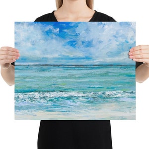 Op de afbeelding: Een schilderij van een zeelandschap met een blauwe lucht en witte wolken. De oceaan is turquoise blauw met witte golven die breken op de kust. Het zand is licht beige.