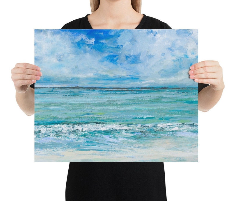 Op de afbeelding: Een schilderij van een zeelandschap met een blauwe lucht en witte wolken. De oceaan is turquoise blauw met witte golven die breken op de kust. Het zand is licht beige.