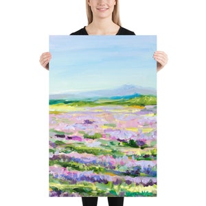 Op de afbeelding: Een schilderij van een veld met paarse bloemen met een bergketen op de achtergrond. De lucht is blauw en de bloemen zijn geschilderd in een losse, impressionistische stijl.