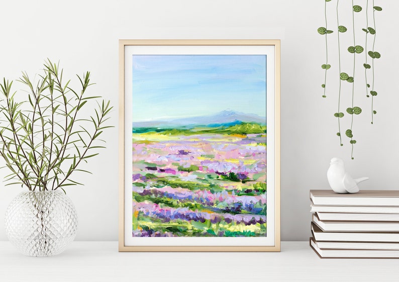 Op de afbeelding: Een ingelijst schilderij van een lavendelveld met een bergketen op de achtergrond. Het schilderij is gemaakt in een losse, impressionistische stijl met felle kleuren.