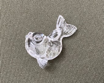 May include: A clear glass figurine of a fish with a detailed design. The fish has a rounded body and a tail fin.
