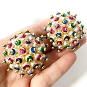 May include: A pair of large, round earrings made of white pearls and colourful sequins. The earrings are clustered together in a sphere shape.