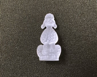 May include: A clear, poodle-shaped charm. The charm is made of a translucent material and features a detailed poodle design. The poodle is sitting, with its head and ears clearly defined. The charm is a decorative item.