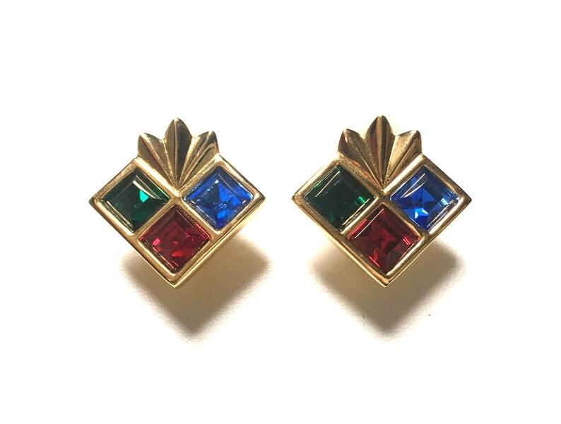 Puede incluir: Un par de pendientes de tono dorado con un dise&ntilde;o geom&eacute;trico. Cada pendiente presenta cuatro piedras de forma cuadrada en rojo, verde y azul.