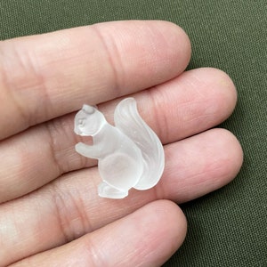 May include: A clear glass squirrel figurine. The squirrel is sitting on its haunches with its tail curled behind it.