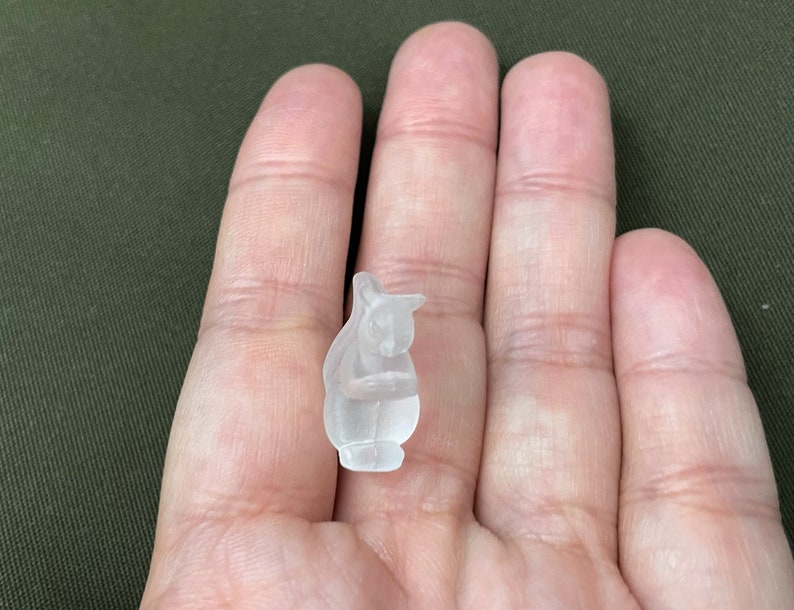 May include: A small, clear glass figurine of a squirrel sitting on its hind legs, holding a nut in its paws.