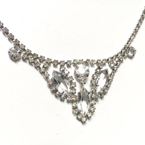 May include: A silver necklace with a delicate chain and a large, sparkling rhinestone pendant. The pendant features a cluster of marquise-shaped rhinestones.