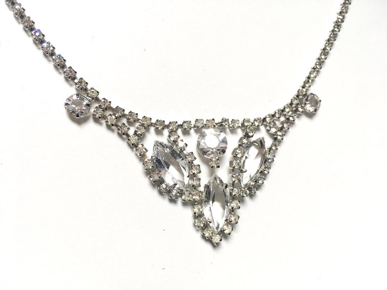 May include: A silver necklace with a delicate chain and a large, sparkling rhinestone pendant. The pendant features a cluster of marquise-shaped rhinestones.