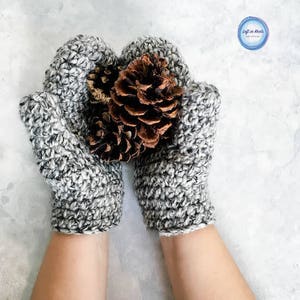 May include: A pair of gray and white crocheted mittens with a pine cone in the center.