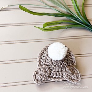 Puede incluir: Un conejito de crochet marr&oacute;n con una cola de pomp&oacute;n blanco. El conejito est&aacute; acostado sobre una superficie de madera marr&oacute;n claro. &copy; Left in Knots www.leftinknots.com