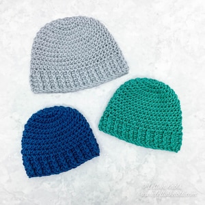 May include: Three crocheted hats in different colors: gray, teal, and blue. The hats are all made with the same stitch pattern and have a simple, classic design.