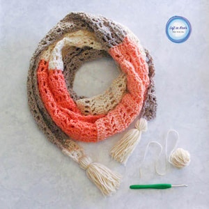 Może przedstawiać: Szalik szydełkowy z przejściem kolorystycznym od brzoskwiniowego, przez kremowy, do brązowego. Szalik ma dwie frędzle i leży na białym tle z kłębkiem włóczki, szydełkiem i kawałkiem włóczki.