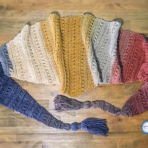 May include: A crocheted scarf with a gradient of blue, beige, yellow, grey, and red. The scarf has long tassels on each end.