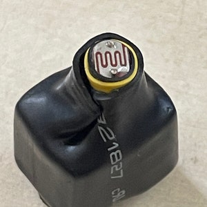 May include: A black electronic component with a yellow ring and a silver top featuring a red, wavy design. The component is encased in a black, heat-shrinkable sleeve. The text "21827" is printed on the side.