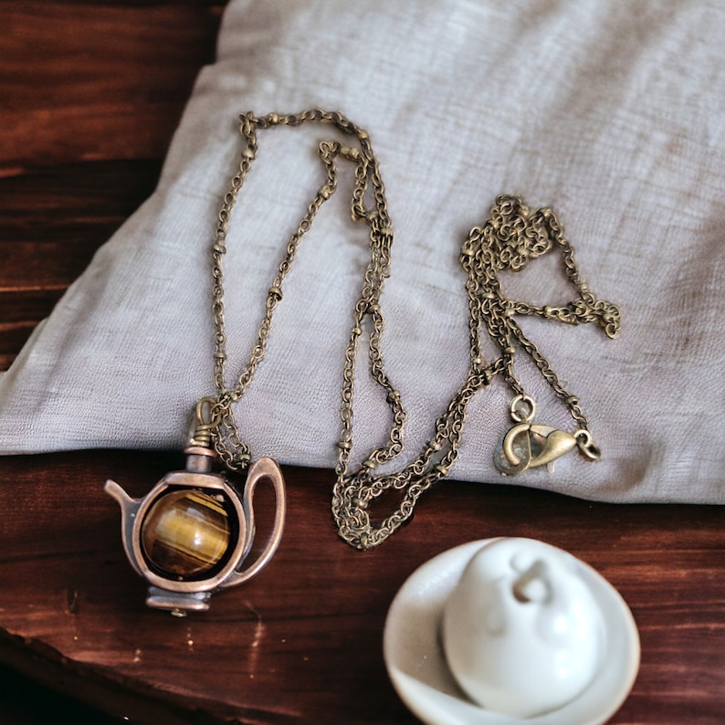 May include: A gold chain necklace with a teapot pendant featuring a tiger's eye stone.