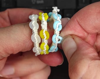 May include: Three rings made of white cord woven with small circular beads. One ring features translucent white beads, one features bright yellow beads, and one features light blue beads. The rings are constructed with a knotted cord design.