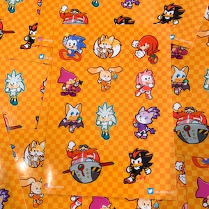 Op de afbeelding: Een vel stickers met verschillende personages uit de Sonic the Hedgehog-franchise. De stickers zijn op een feloranje achtergrond met een geruit patroon. De personages zijn Sonic, Tails, Knuckles, Amy, Shadow, Rouge en Eggman.