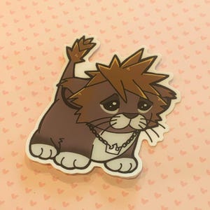 May include: A sticker featuring a cartoon lion with brown fur, a spiky brown hairstyle, and a silver necklace. The lion has a sad expression and white paws. The sticker is on a pink background with small heart shapes.