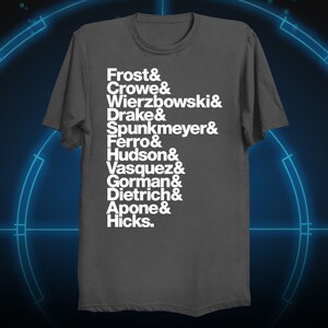 May include: A dark gray t-shirt with white text listing the names Frost, Crowe, Wierzbowski, Drake, Spunkmeyer, Ferro, Hudson, Vasquez, Gorman, Dietrich, Apone, and Hicks.