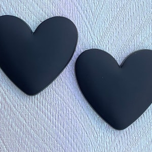 May include: Two black heart-shaped decorations. The hearts are smooth and have a matte finish.