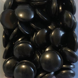 May include: A collection of smooth, black, round stones. Each stone has a flat bottom and a slightly domed top, with a glossy finish. The stones are piled together, creating a dense, textured appearance. The color is a deep, solid black.