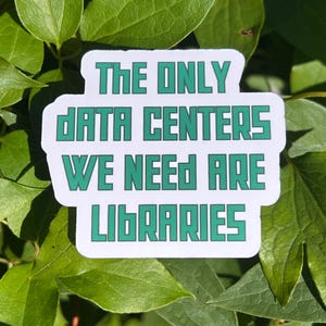 May include: A white die-cut sticker with a teal-colored, blocky, sans-serif font that reads: THE ONLY DATA CENTERS WE NEED ARE LIBRARIES. The sticker has a smooth, rounded rectangular shape and is positioned against a background of green leaves.