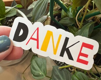 May include: A white sticker with the word "DANKE" written in black, red, and yellow letters. The letters are stylised and outlined in black.