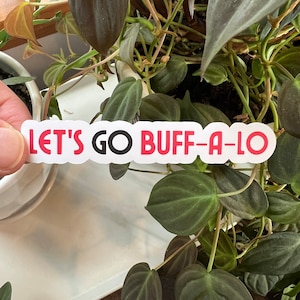 May include: White sticker with the text "Let's Go Buff-a-lo" in red letters with a black circle for the "O" in "Go".