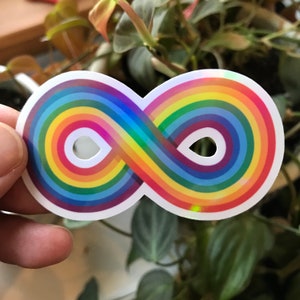 May include: A rainbow infinity symbol sticker with a holographic finish. The sticker is white with a rainbow design.