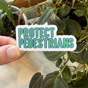 May include: White sticker with blue and green text that reads "PROTECT PEDESTRIANS".