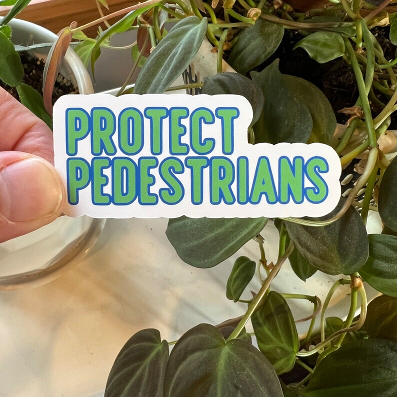 May include: White sticker with blue and green text that reads "PROTECT PEDESTRIANS".
