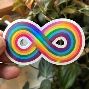 May include: A rainbow infinity symbol sticker with a holographic finish. The sticker is on a white background.