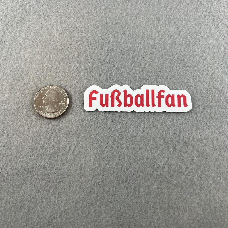 May include: White sticker with the red text "Fu&szlig;ballfan" on a gray surface.