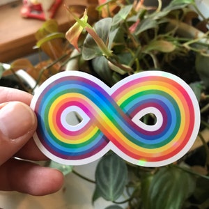 May include: A rainbow infinity symbol sticker with a holographic finish. The sticker is on a white background.