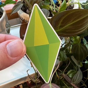 May include: A green and yellow diamond-shaped sticker with a white outline. The sticker is a popular symbol from the video game The Sims.
