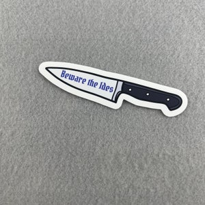 May include: A white sticker with a black and silver knife illustration. The knife has the text "Beware the Ides" written on the blade.